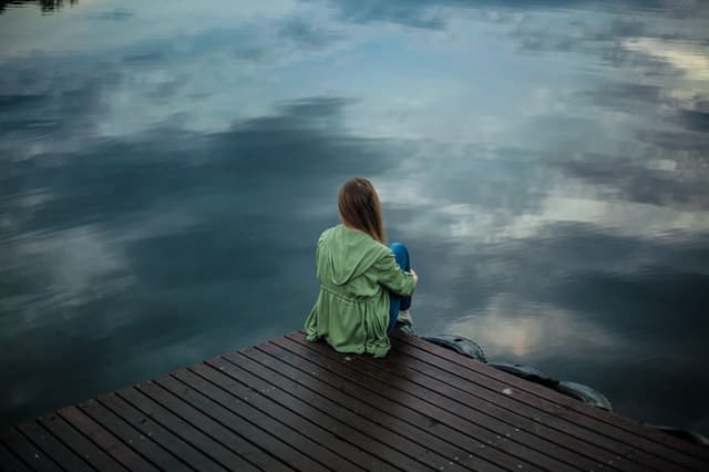 一个女人坐在码头边上，看着水面。