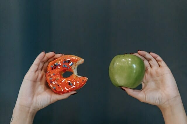 两只手，一只拿着苹果，另一只拿着甜甜圈
